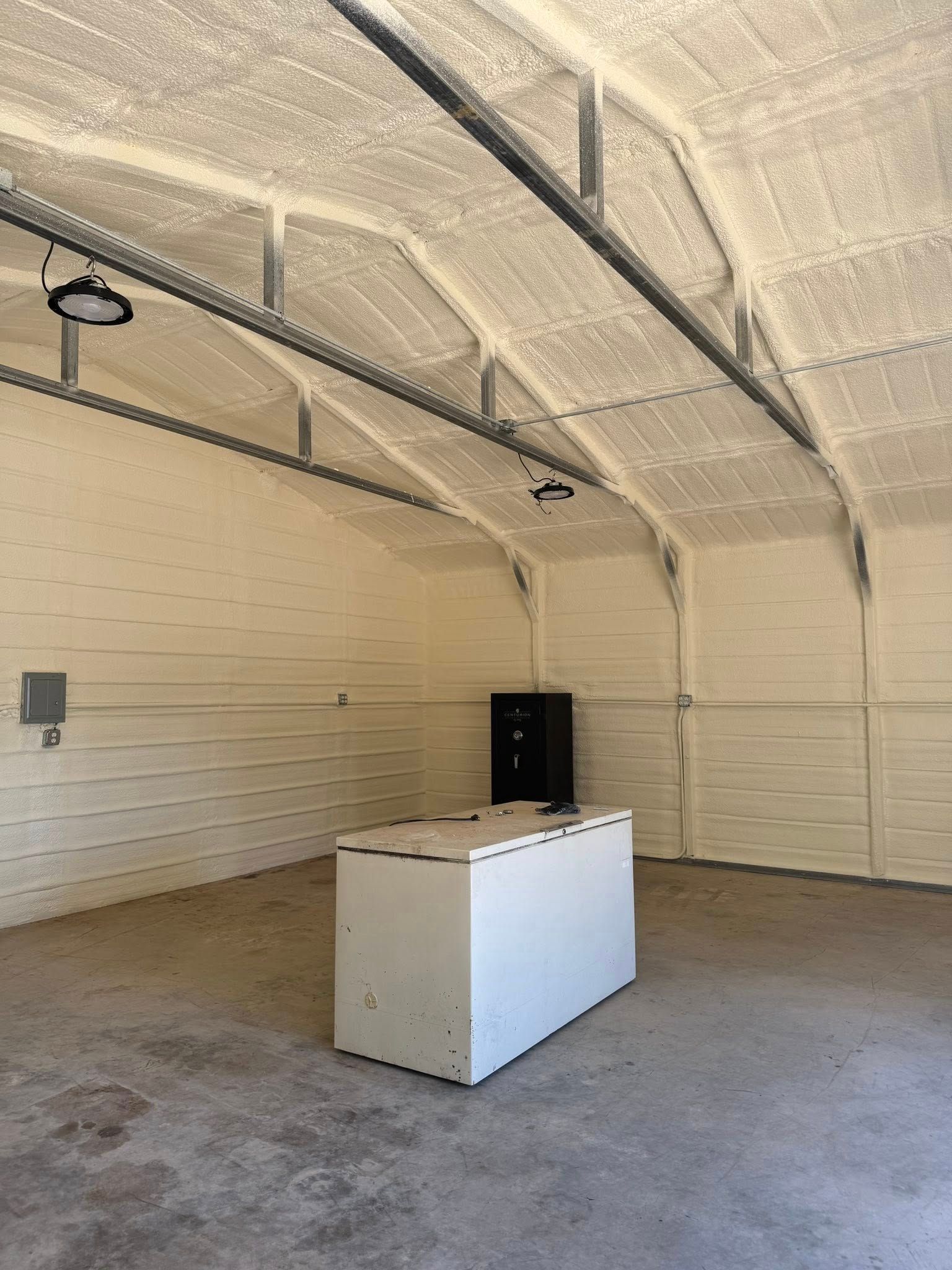 Interior of a building with white foam insulation on the walls and ceiling, a gray floor, and a white cabinet.