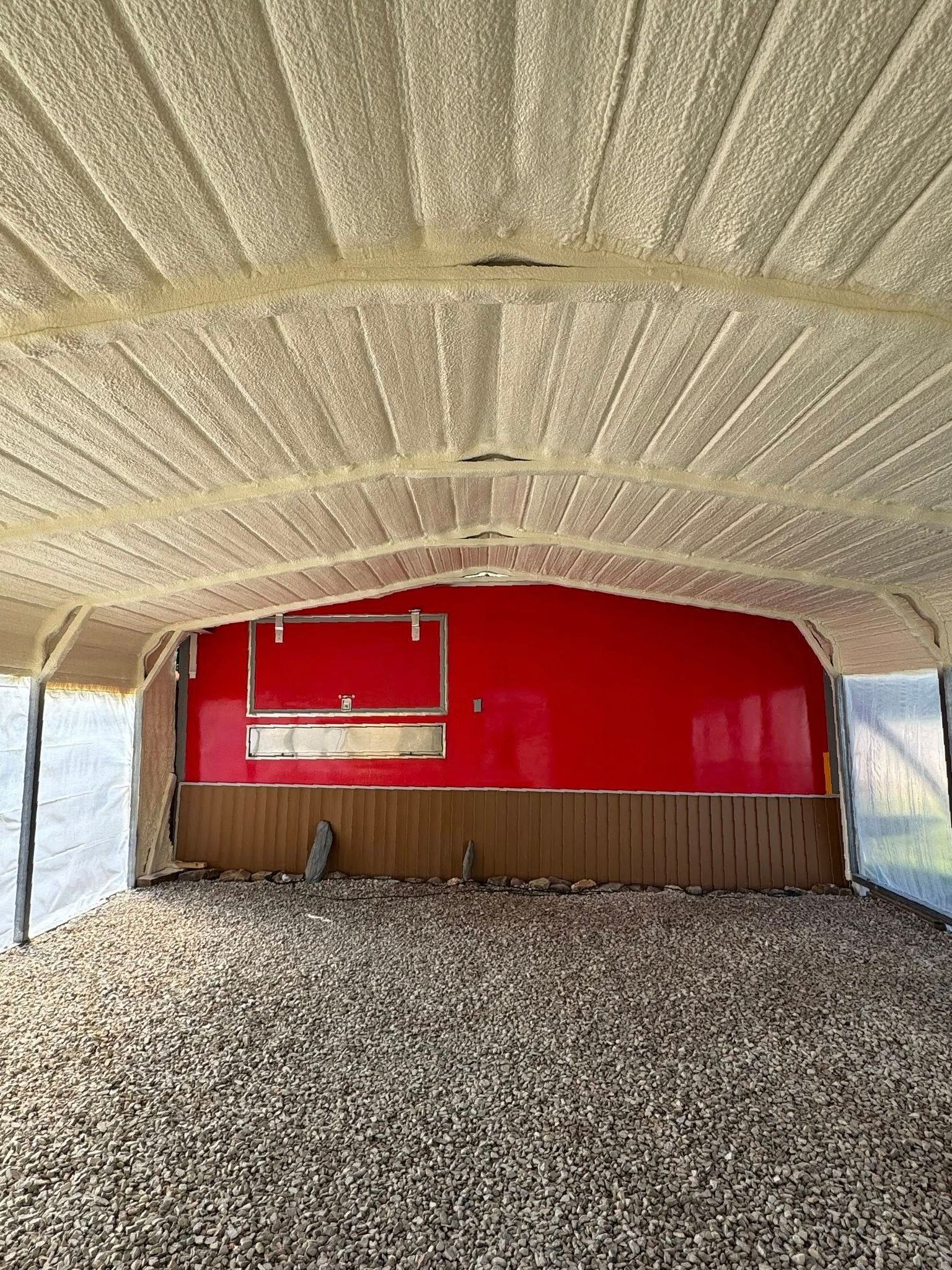 Interior of a building with a red back wall, gravel floor, and a textured, light-colored ceiling.