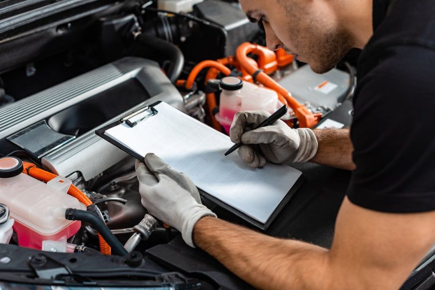 Ein Mechaniker untersucht in einer Garage mit Klemmbrett und Tablet und trägt dabei Handschuhe.