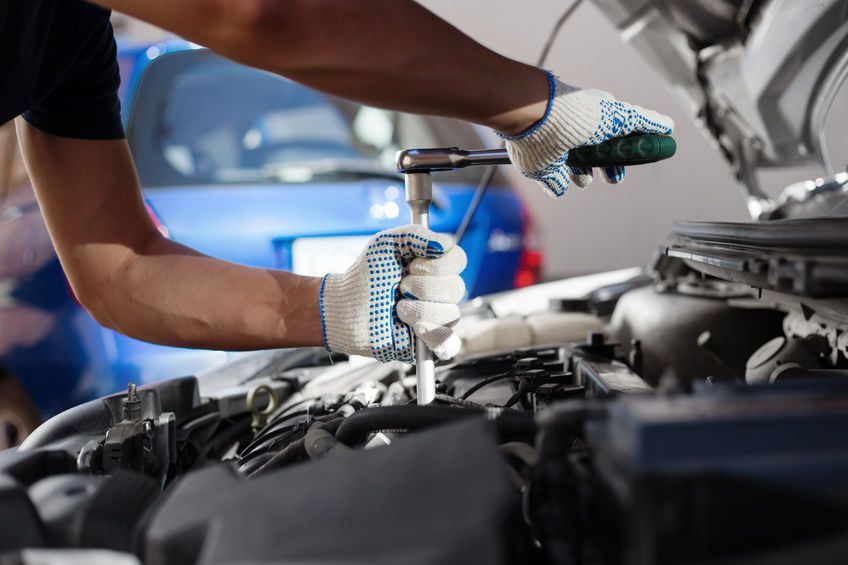 Ein Mechaniker benutzt einen Schraubenschlüssel, um in einer Garage an einem Automotor zu arbeiten.