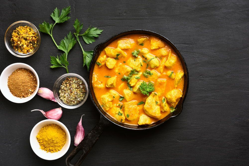 A Skillet Filled With Chicken Curry Next To Bowls Of Spices — Punjabi Sunrise In Alexandra Hills, QLD