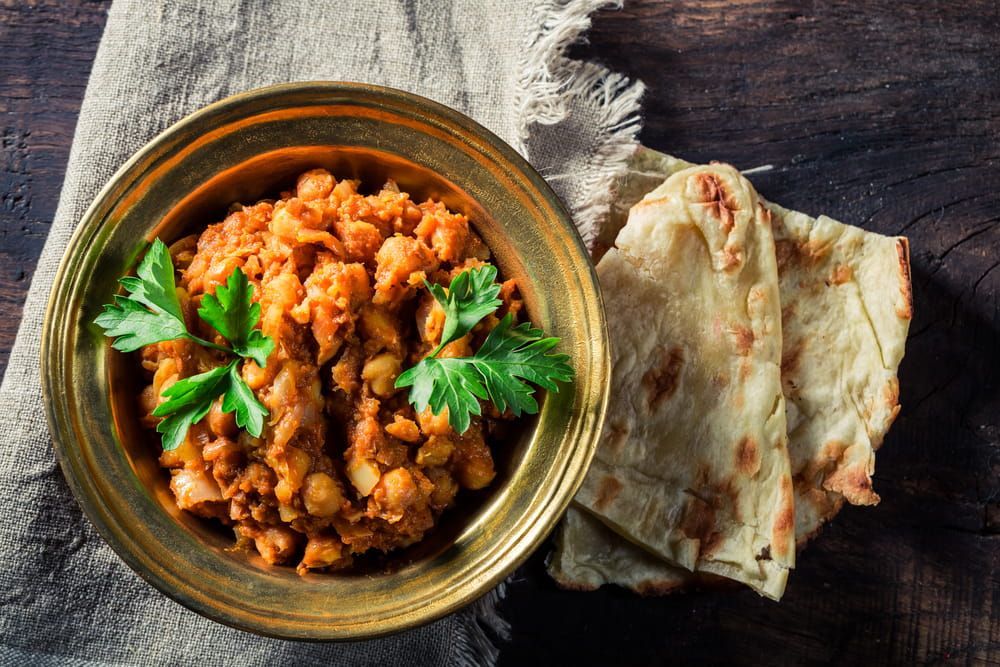 A Bowl Of Indian Food Next To A Piece Of Naan Bread On A Wooden Table — Punjabi Sunrise Restaurant In Alexandra Hills, QLD