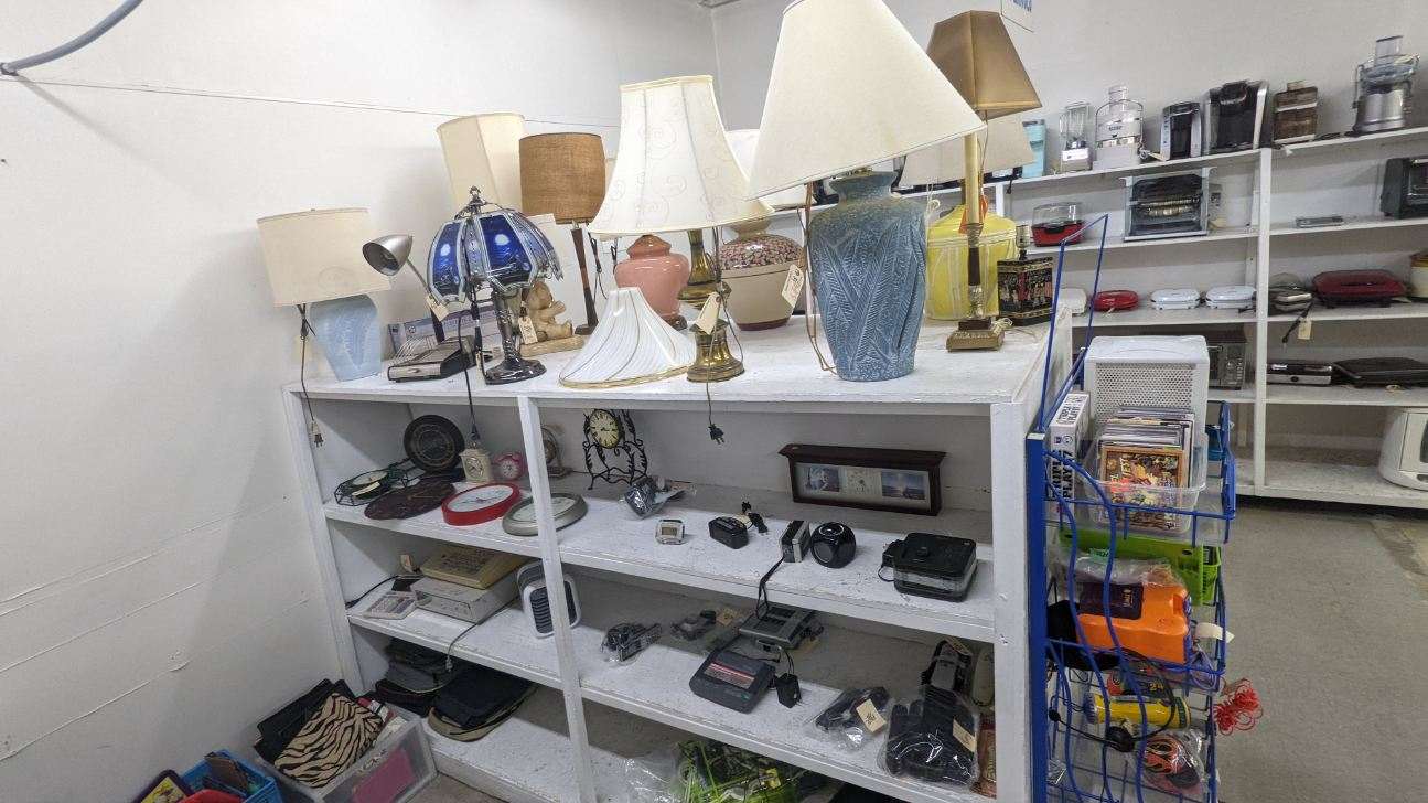 Shelves in a thrift store, filled with lamps and small electronics.
