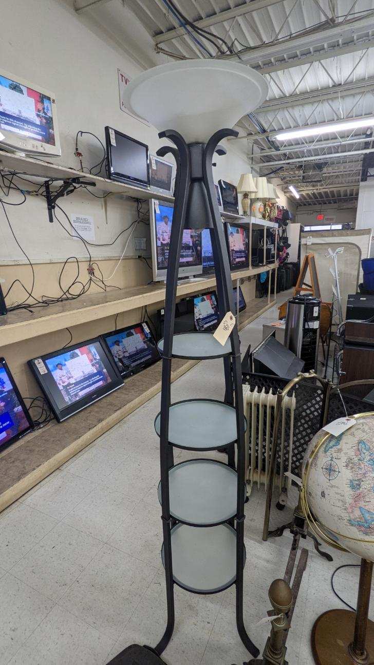 Black floor lamp with shelves in a store, surrounded by televisions and other items.