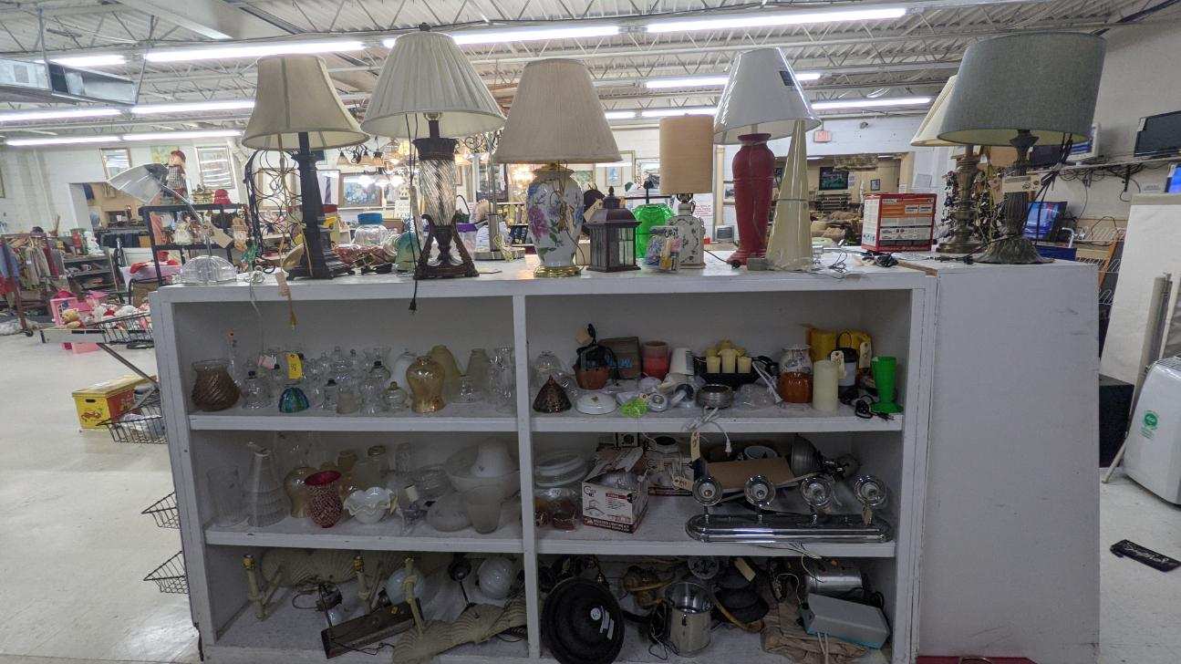 Lamps and knick-knacks displayed on white shelves in a brightly lit store with other items in the background.