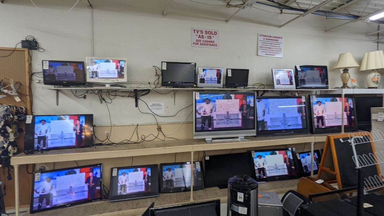 Televisions for sale on shelves in a store. Some are on, displaying images.