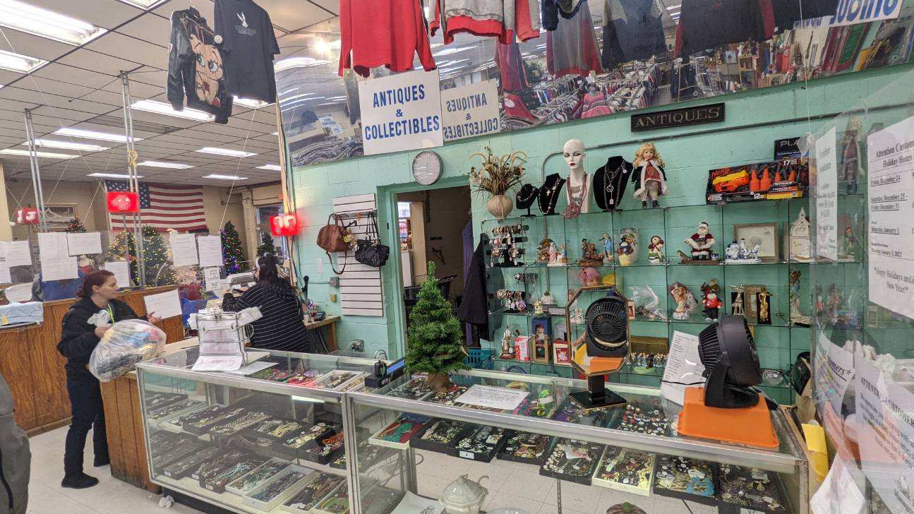 Inside a shop with merchandise on display. A customer stands near the counter. Shelves display trinkets.