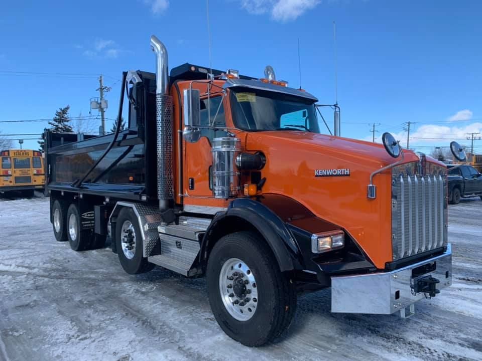 Camion à benne basculante Kenworth orange sur un terrain enneigé.