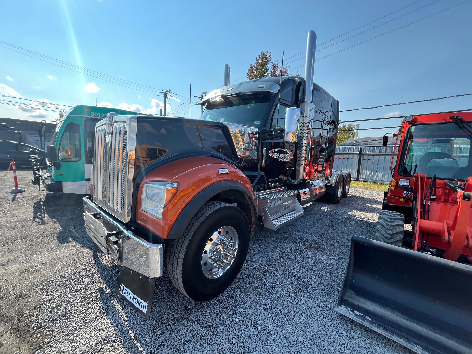 Semi-camion noir et orange garé à l'extérieur par une journée ensoleillée.