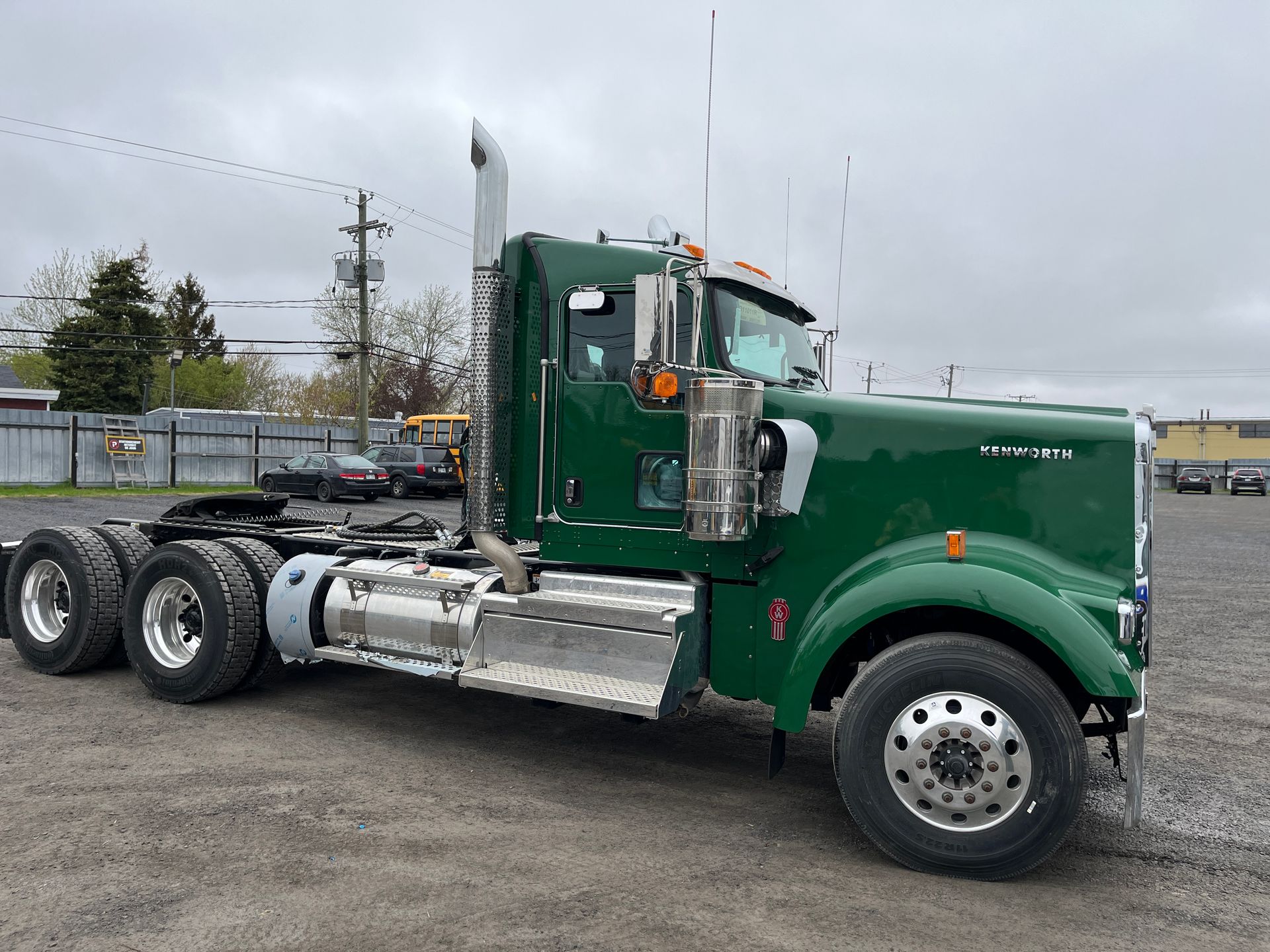 Semi-remorque Kenworth verte stationnée à l'extérieur. Réservoirs de carburant et pot d'échappement argentés, ciel nuageux.