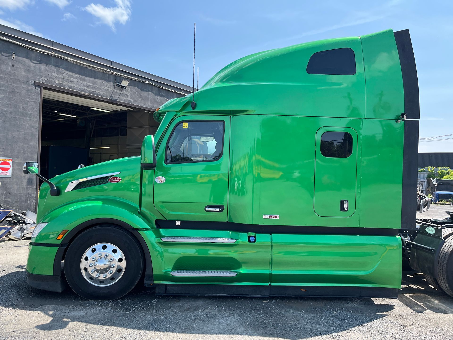 Un semi-remorque vert est stationné près d'un bâtiment par une journée ensoleillée.