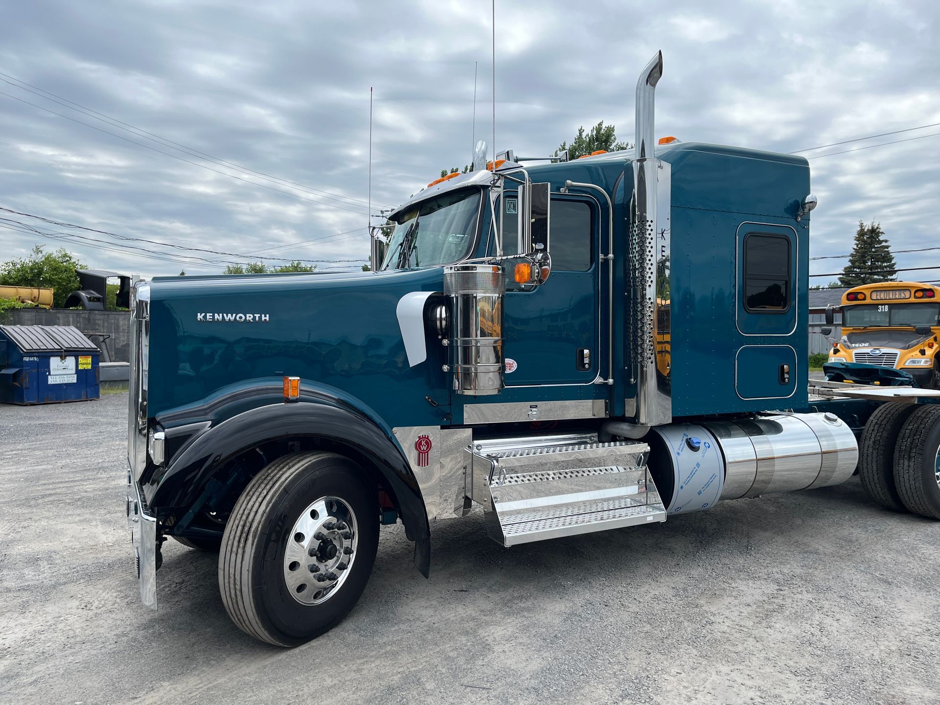 Un semi-remorque bleu foncé est garé à l'extérieur par temps nuageux, avec des accents chromés et un gros pot d'échappement.