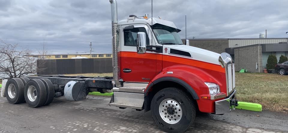 Camion Kenworth rouge et blanc stationné sur l'asphalte. Journée nuageuse.