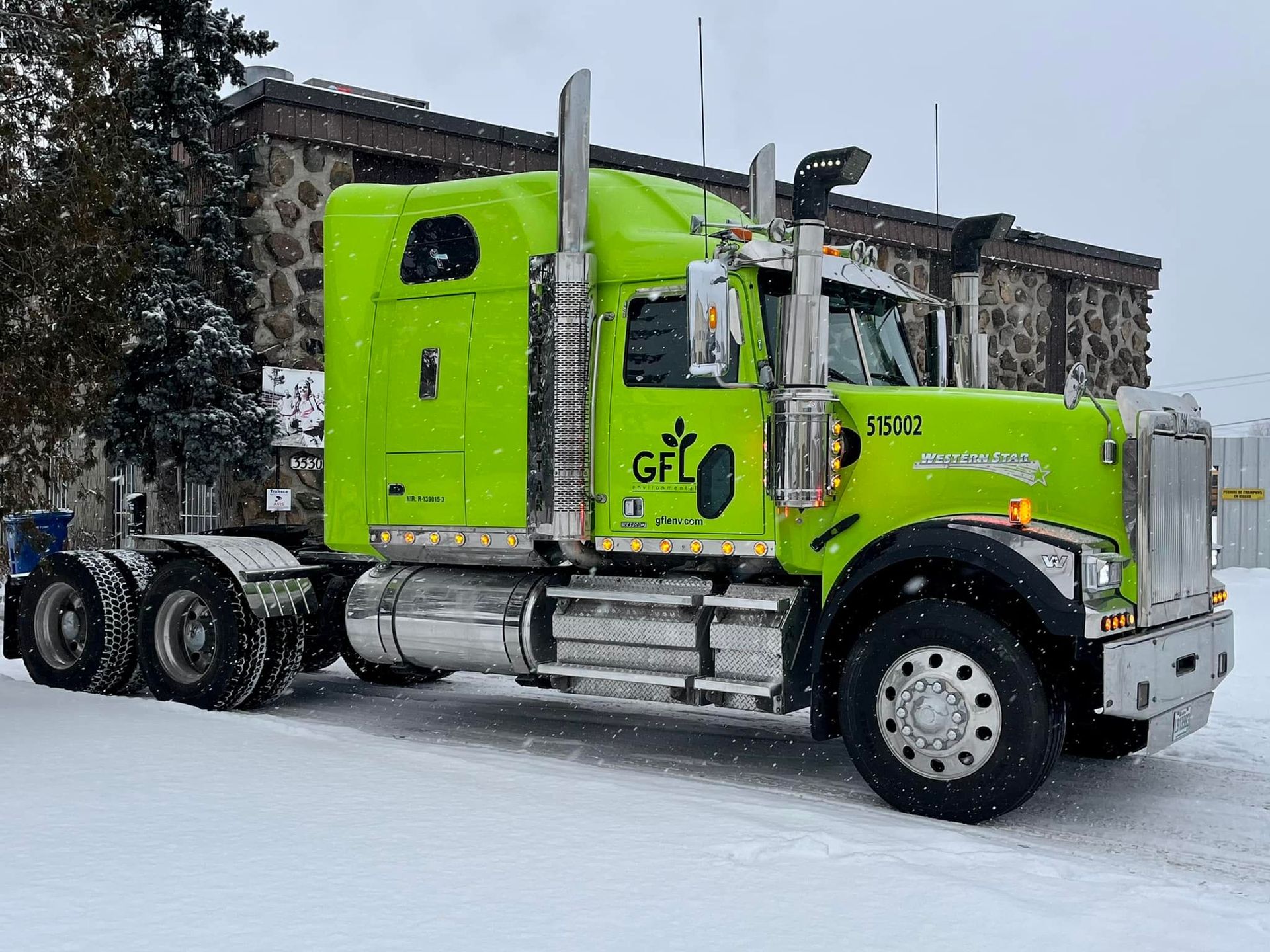 Semi-remorque GFL vert citron stationné dans la neige à côté d'un bâtiment en pierre.