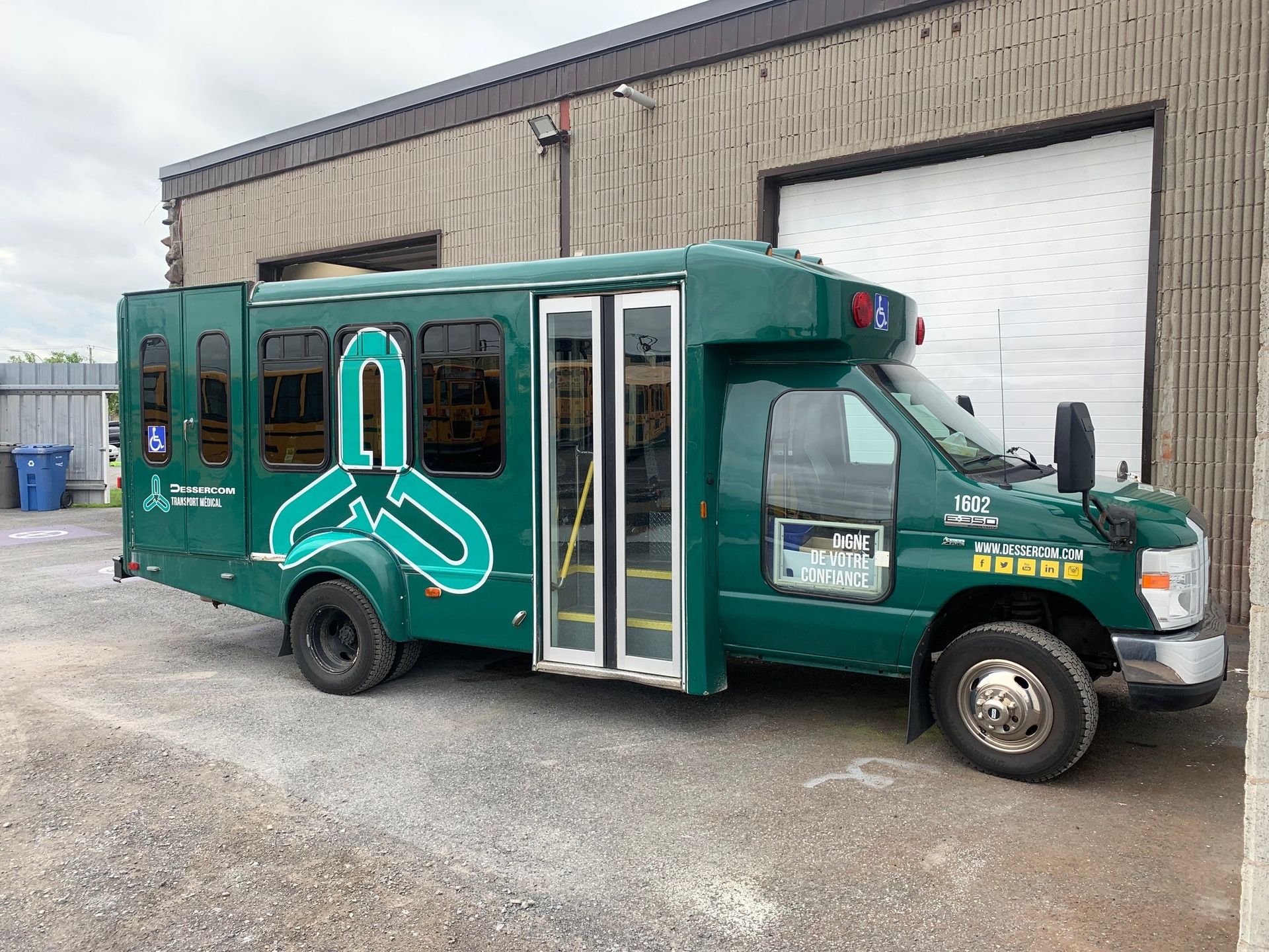 Bus vert accessible aux personnes handicapées, stationné à proximité d'un immeuble.
