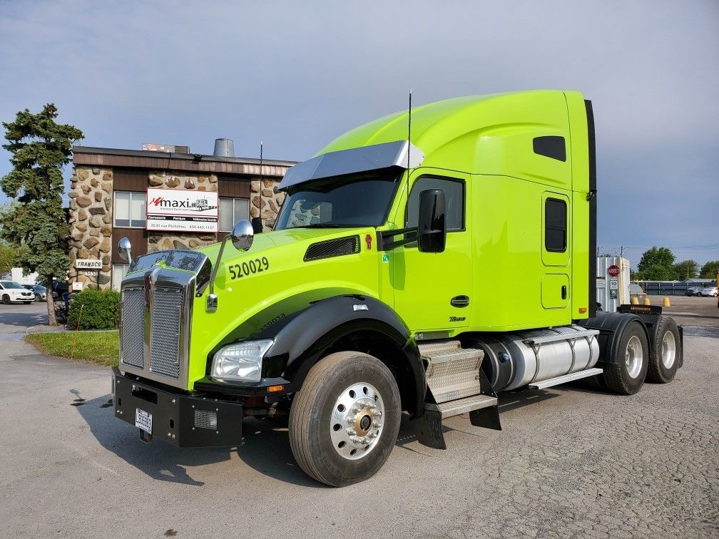 Semi-remorque Kenworth vert vif garé à l'extérieur d'un bâtiment sous un ciel nuageux.