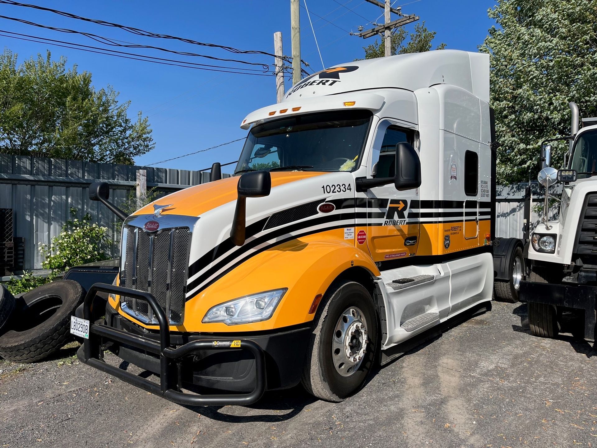 Un semi-remorque jaune et blanc est stationné à l'extérieur par une journée ensoleillée. On distingue un pare-chocs avant de protection et une bande noire.