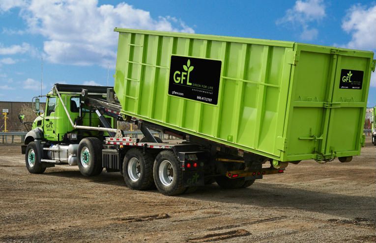 Un camion-benne GFL vert vif sur un terrain vague, se détachant sur un ciel bleu partiellement nuageux.
