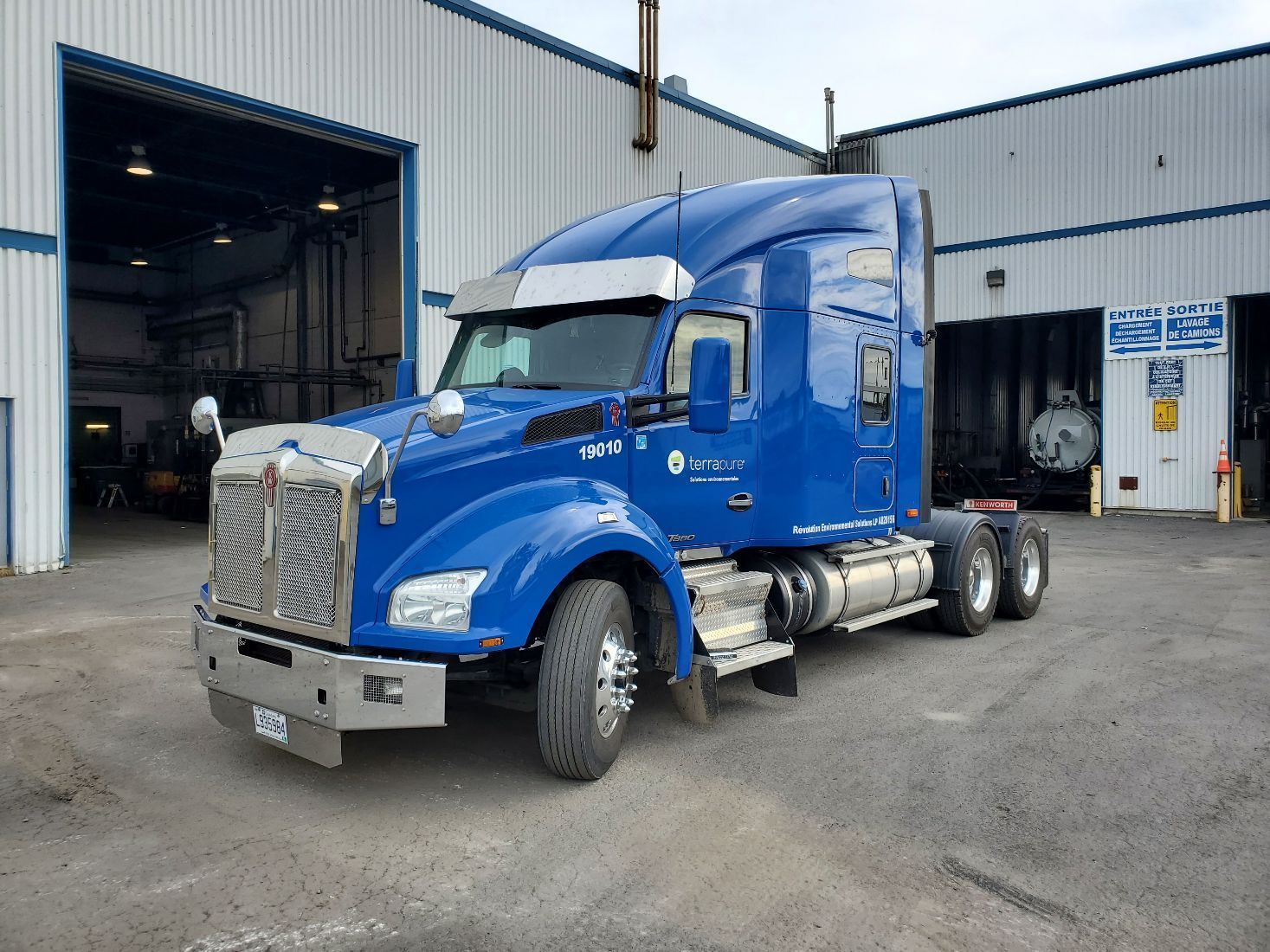 Un semi-remorque Kenworth bleu est garé devant un garage gris.