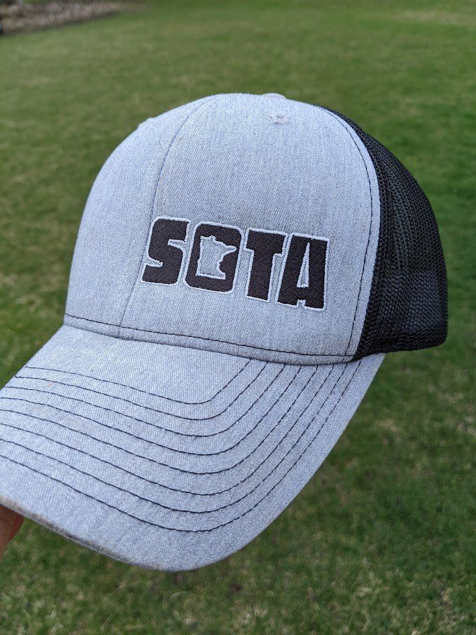 A person is holding a baseball cap with the word sota on it.