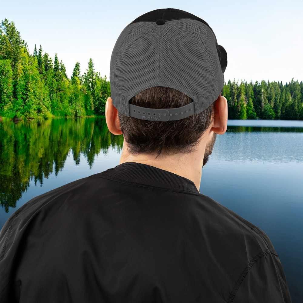 A man wearing a baseball cap is looking at a lake