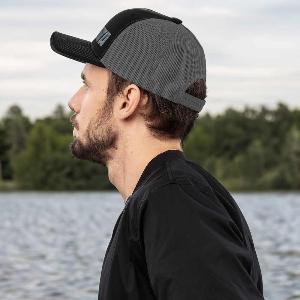 A man wearing a black shirt and a gray hat is standing in front of a body of water