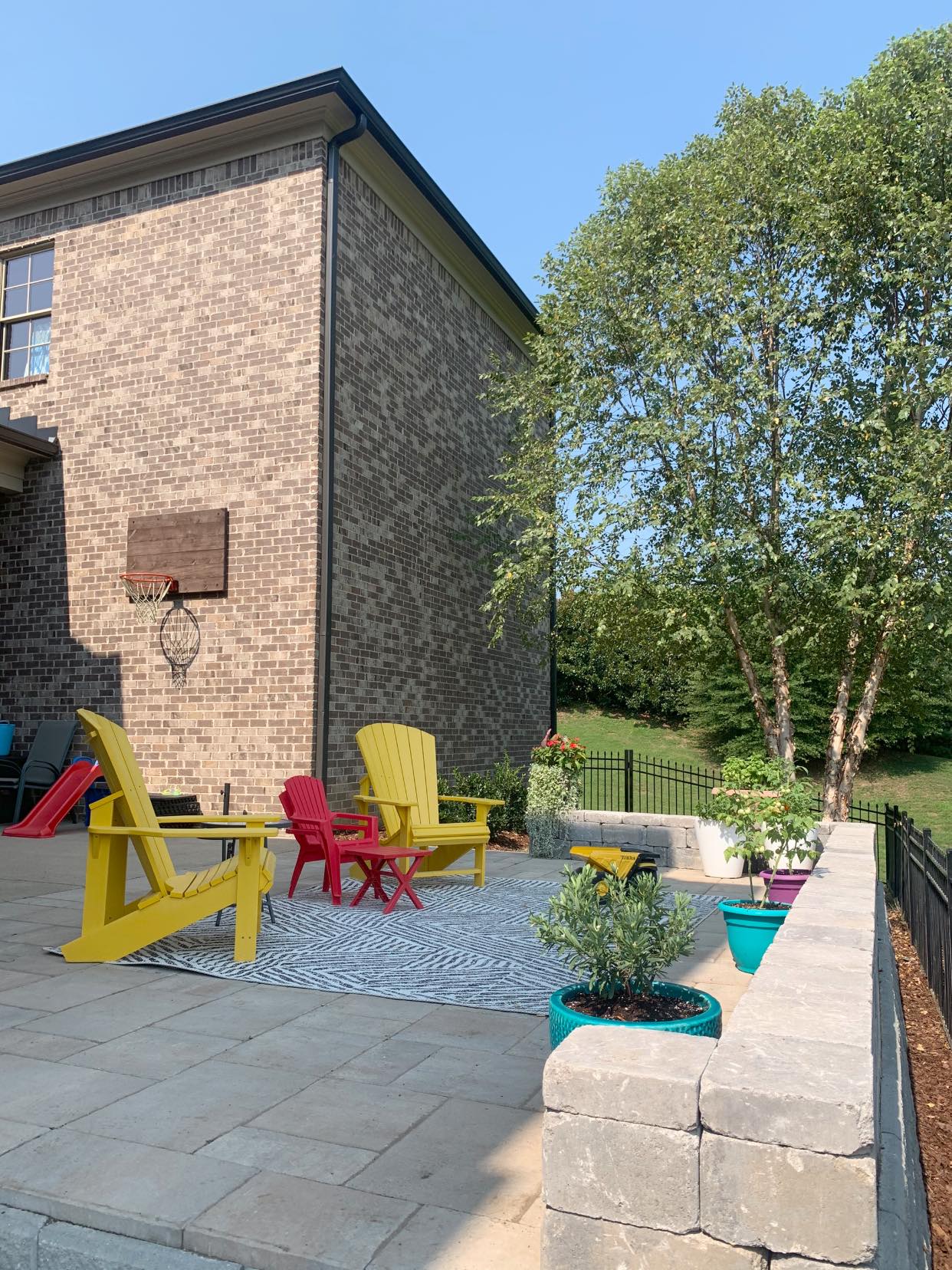 A patio with colorful chairs and a basketball hoop in front of a brick house.