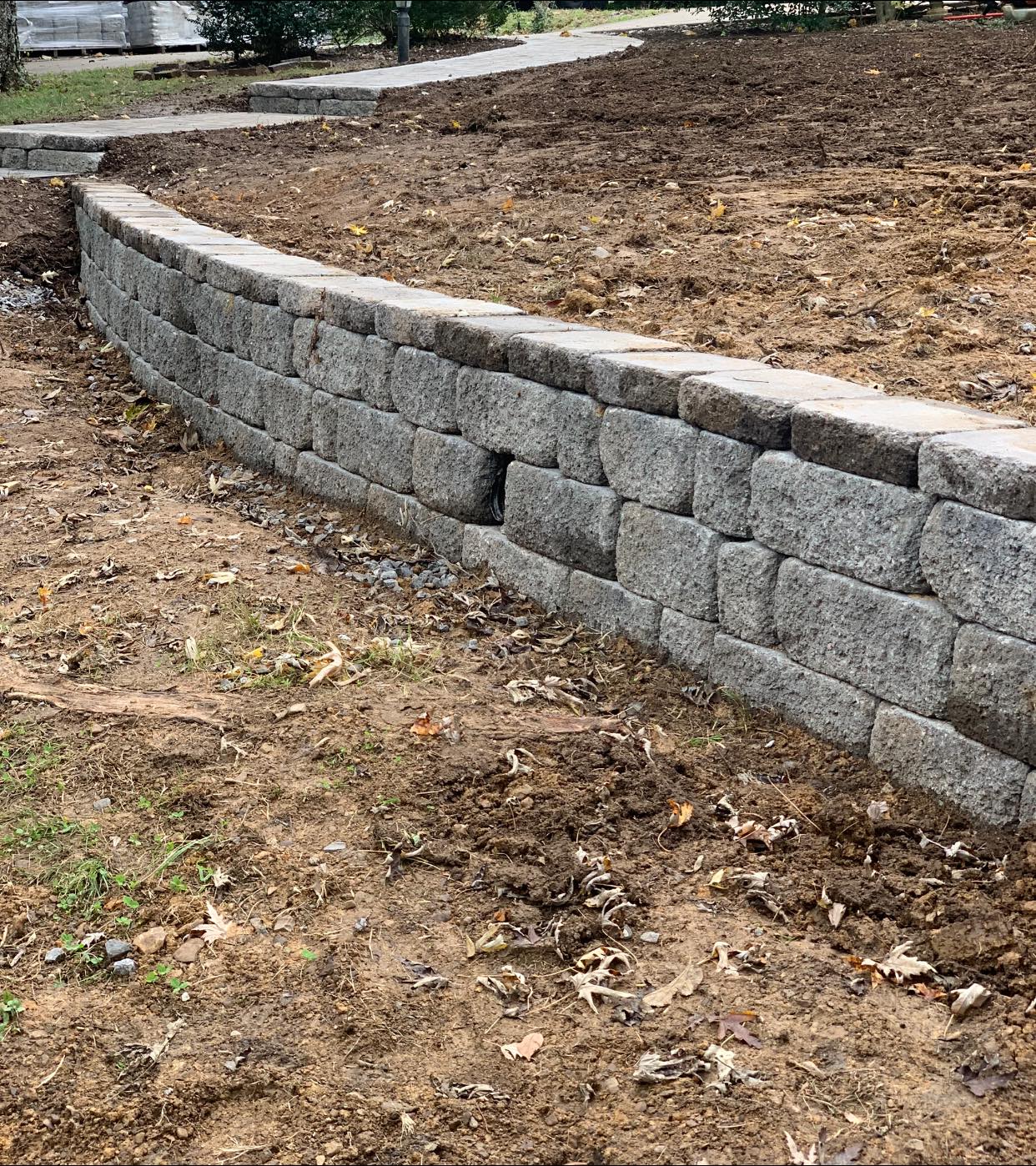 A stone wall is sitting in the middle of a dirt field.