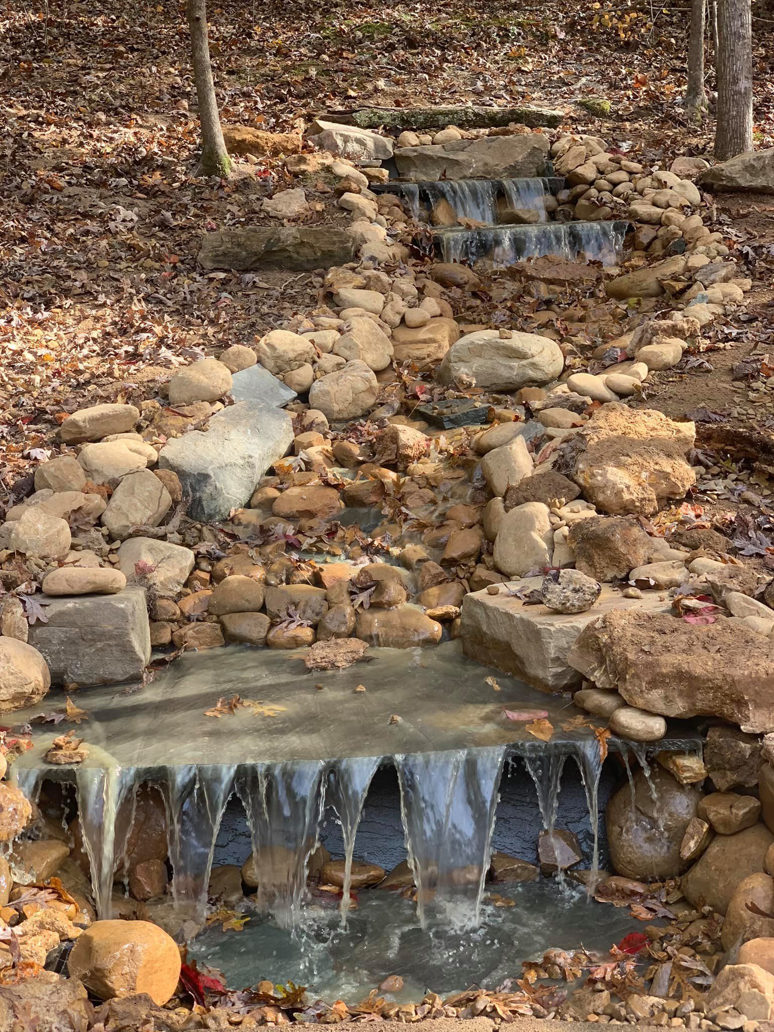 A small waterfall is surrounded by rocks and leaves in the woods.