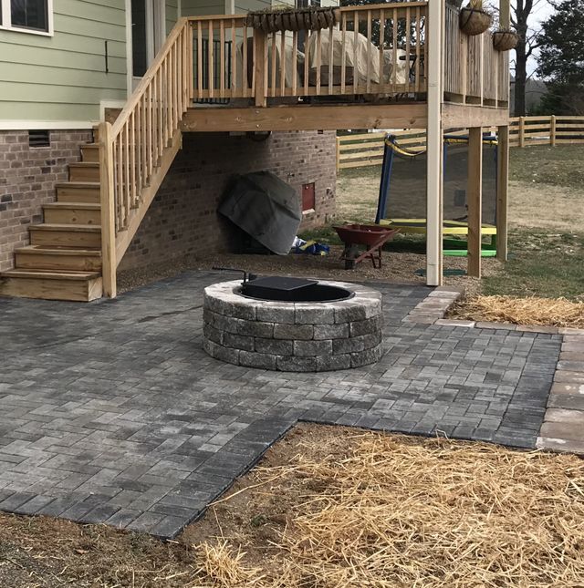 A fire pit on a patio under a deck with stairs