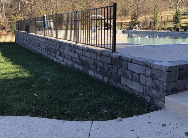 A brick wall surrounds a swimming pool with a metal fence.