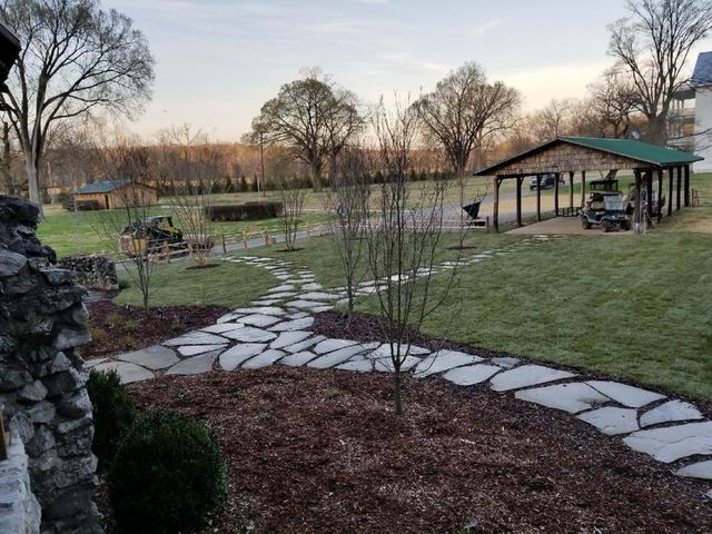 A stone walkway leading to a gazebo in the middle of a grassy field.