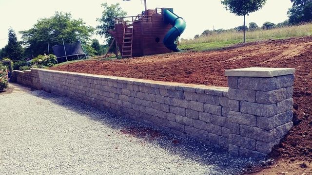 A brick wall surrounding a playground with a slide in the background.