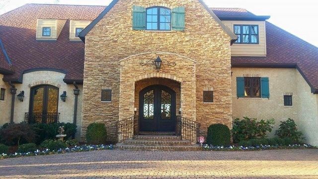 A large brick house with a brown roof and green shutters