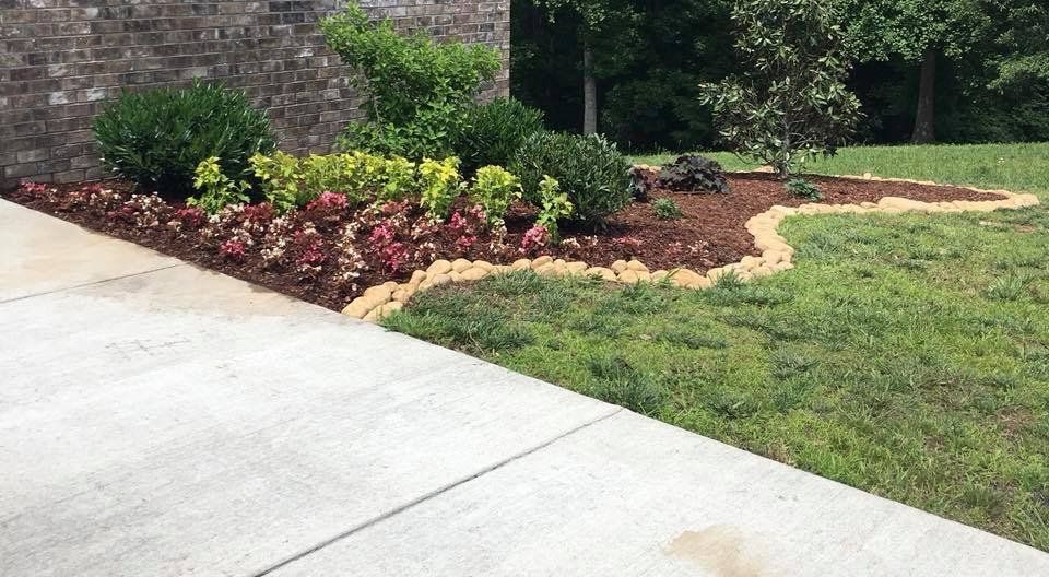 A sidewalk leading to a lush green lawn with a brick wall in the background.