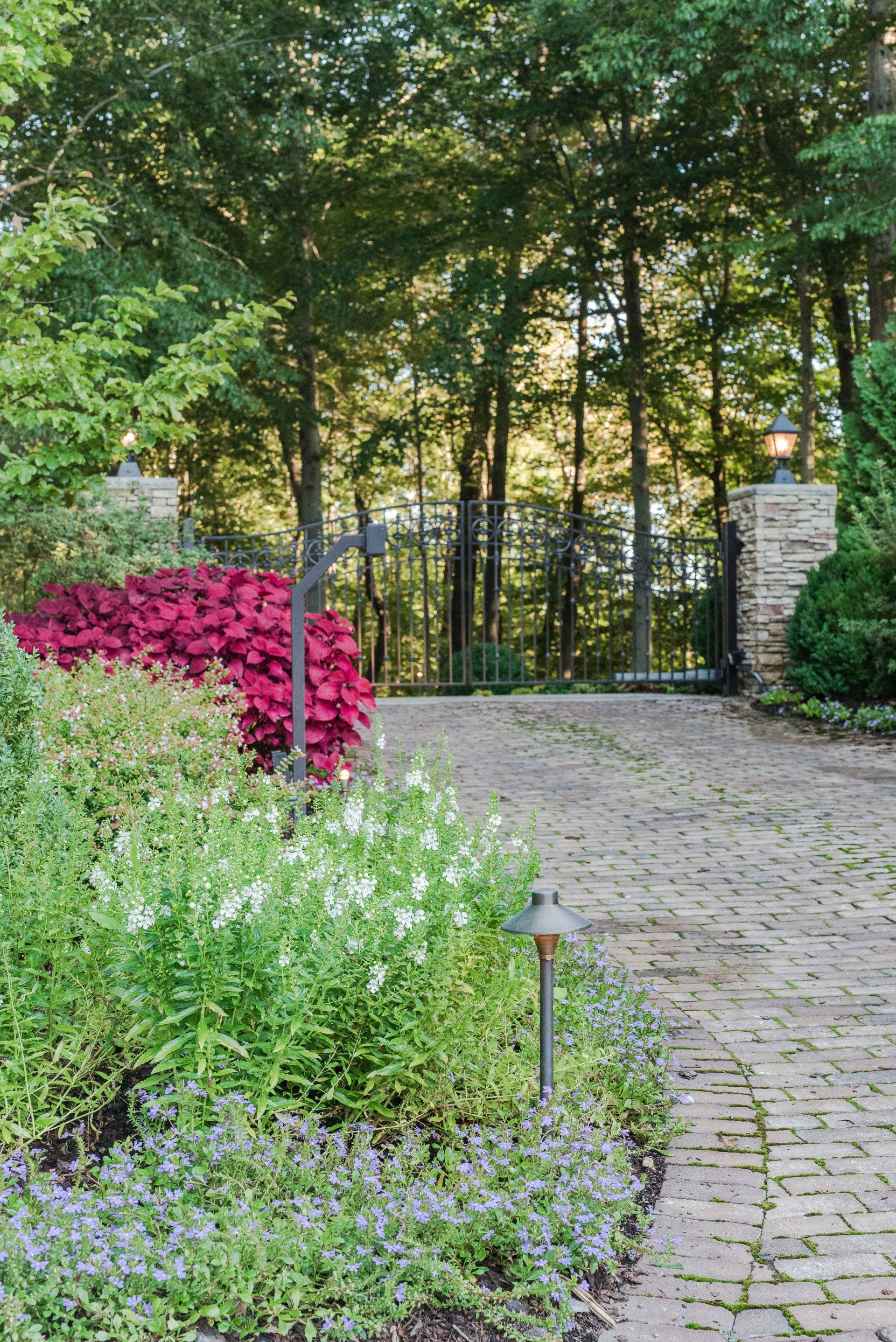 A brick walkway leading to a gate in a garden surrounded by trees.