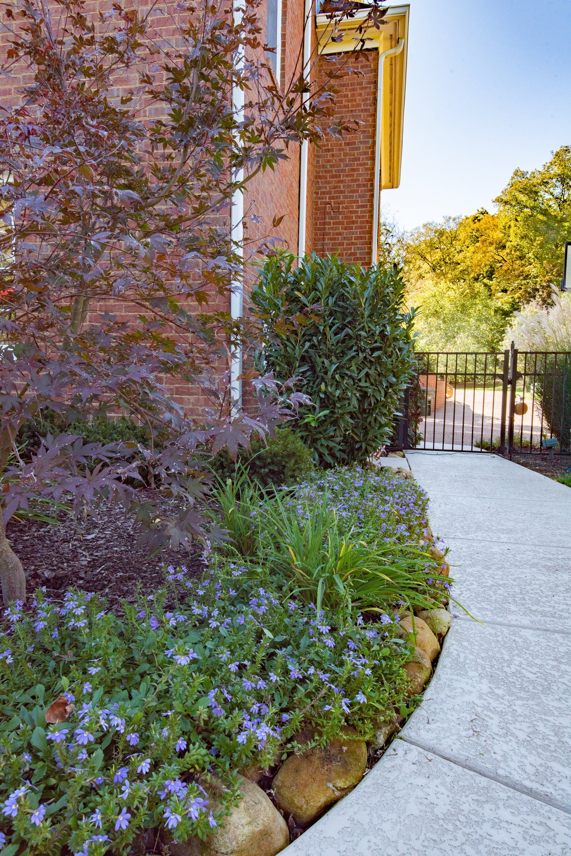 A walkway leading to a brick building with flowers and shrubs on the side.