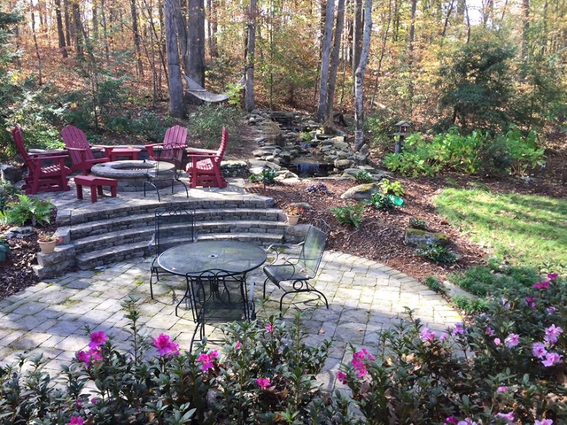 A patio with a table and chairs and a fire pit in the middle of a forest.