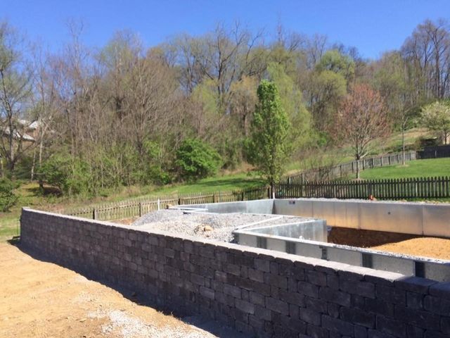 A large brick wall is surrounded by dirt and trees.