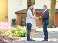 A man and woman are shaking hands with a real estate agent in front of a house.