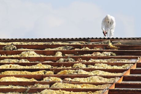 A man in a white suit is working on the roof of a building.