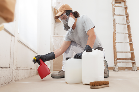 A man wearing a gas mask is spraying a room with a spray bottle.