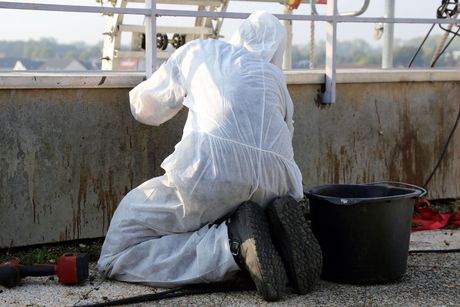 A man in a protective suit is kneeling next to a bucket