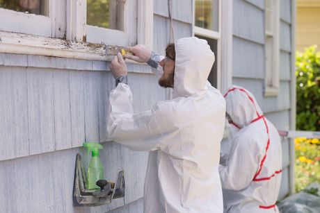 Two men in protective suits are cleaning a window on a house.