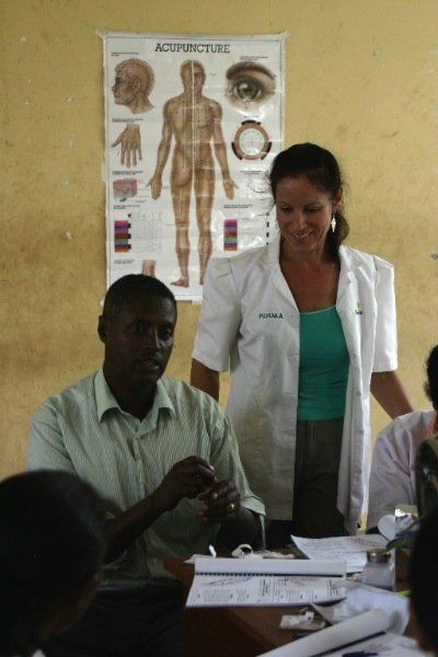 A woman in a lab coat stands in front of a poster of the human body