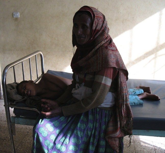 A woman sits next to a sleeping child in a hospital bed