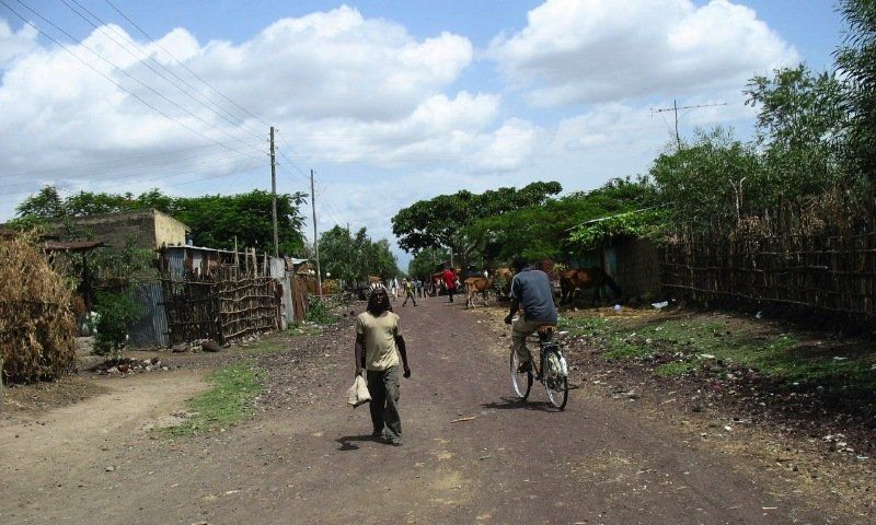A man riding a bike down a dirt road with a woman walking behind him