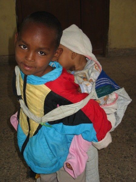 A young boy is carrying a baby on his back