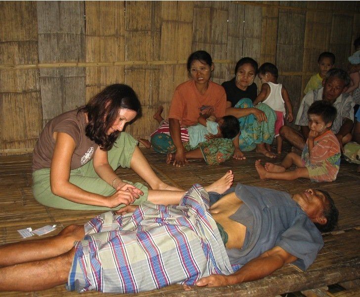 A woman is massaging a man 's foot while a group of people sit around him