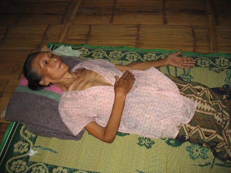 An elderly woman is laying on a mat on the floor